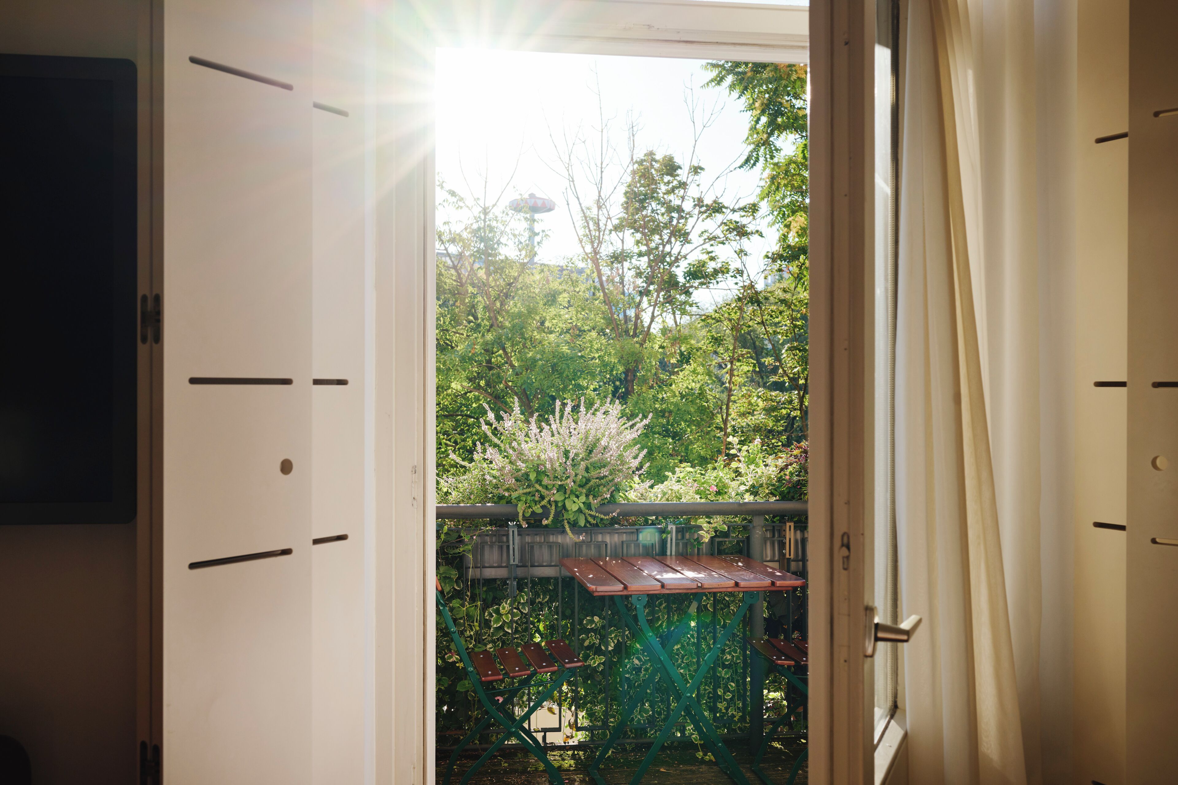 An open door leading to a balcony with a view of greenery and a distant tower.