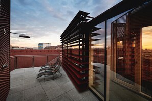 A modern building with a red brick facade, a glass balcony with a metal bench, and a view of the city skyline. - Hotel Weitzer Graz (Graz)