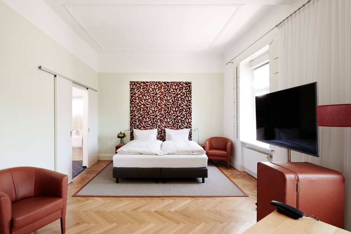 A modern bedroom with a bed, a TV, a desk, and a chair.