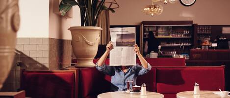 A person reading a menu in a restaurant with red seating, a large potted plant, and a clock on the wall.