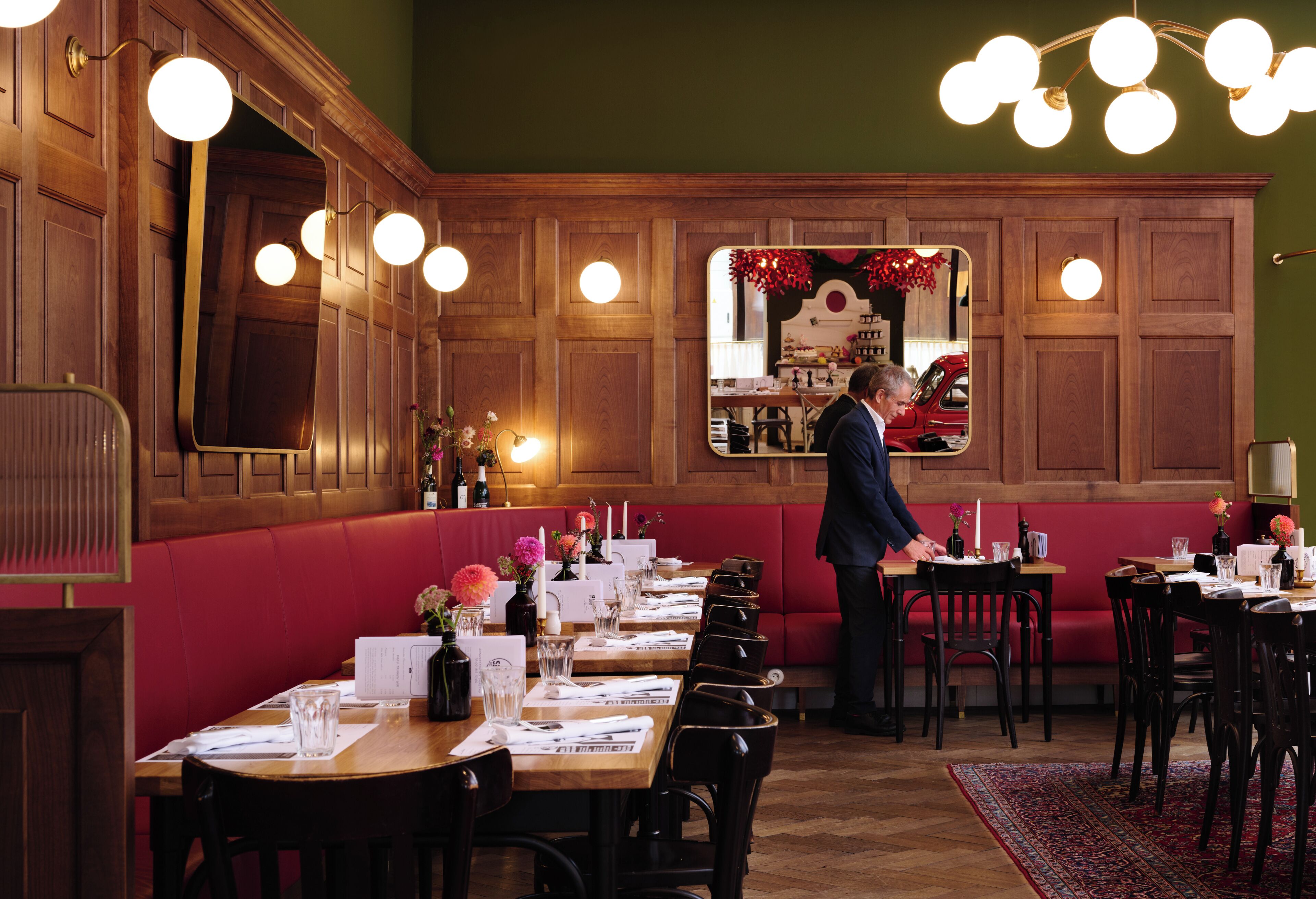 Un restaurante con paneles de madera, cabinas rojas y un hombre de pie junto a la barra.