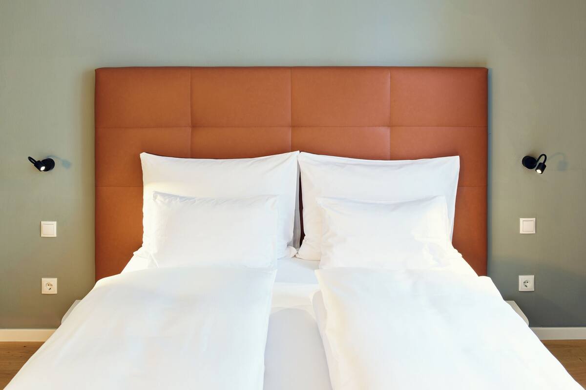 A neatly made bed with white linens in a room with a brown headboard and light green walls.