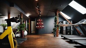 Un gimnasio con equipamiento de ejercicio, suelo de madera, un candelabro y plantas.