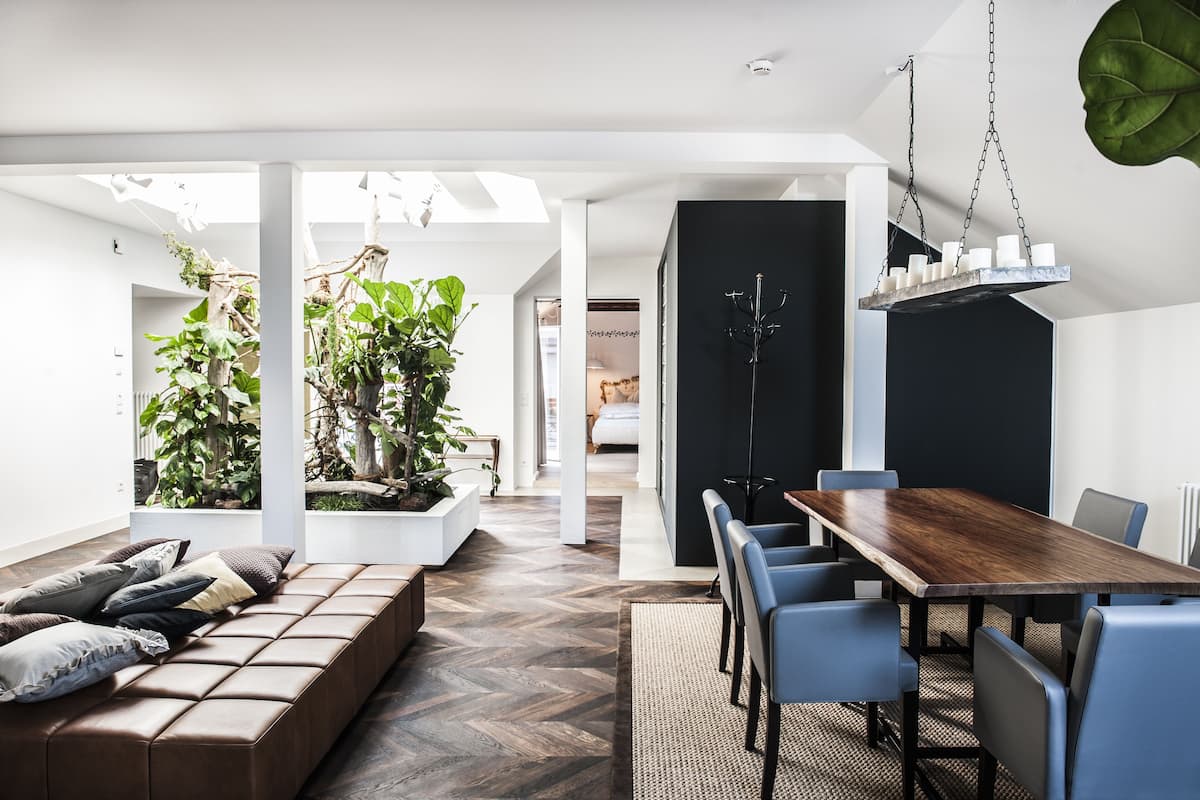 A modern dining area with a wooden table and chairs, a bench with cushions, and potted plants.