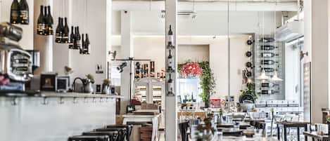 Un interior de restaurante con una zona de bar, mesas para comer y una cocina visible a través de un arco.