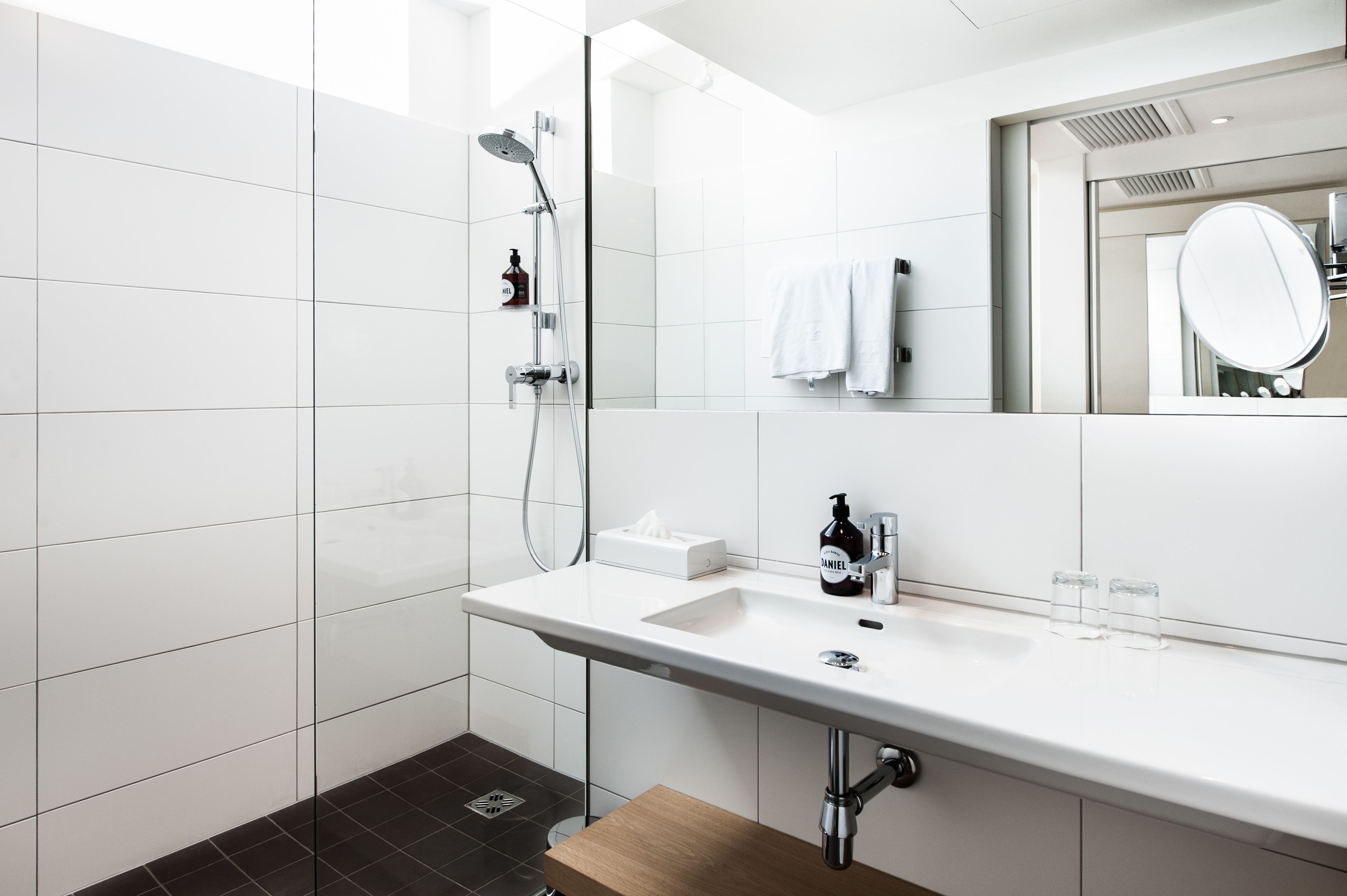 A modern bathroom with a white sink, a mirror, a shower, and a towel rack.