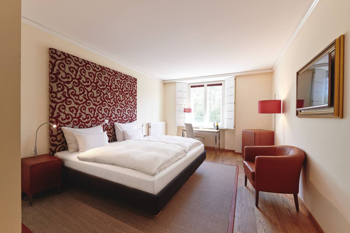 A modern hotel room with a large bed, a desk, and a chair.
