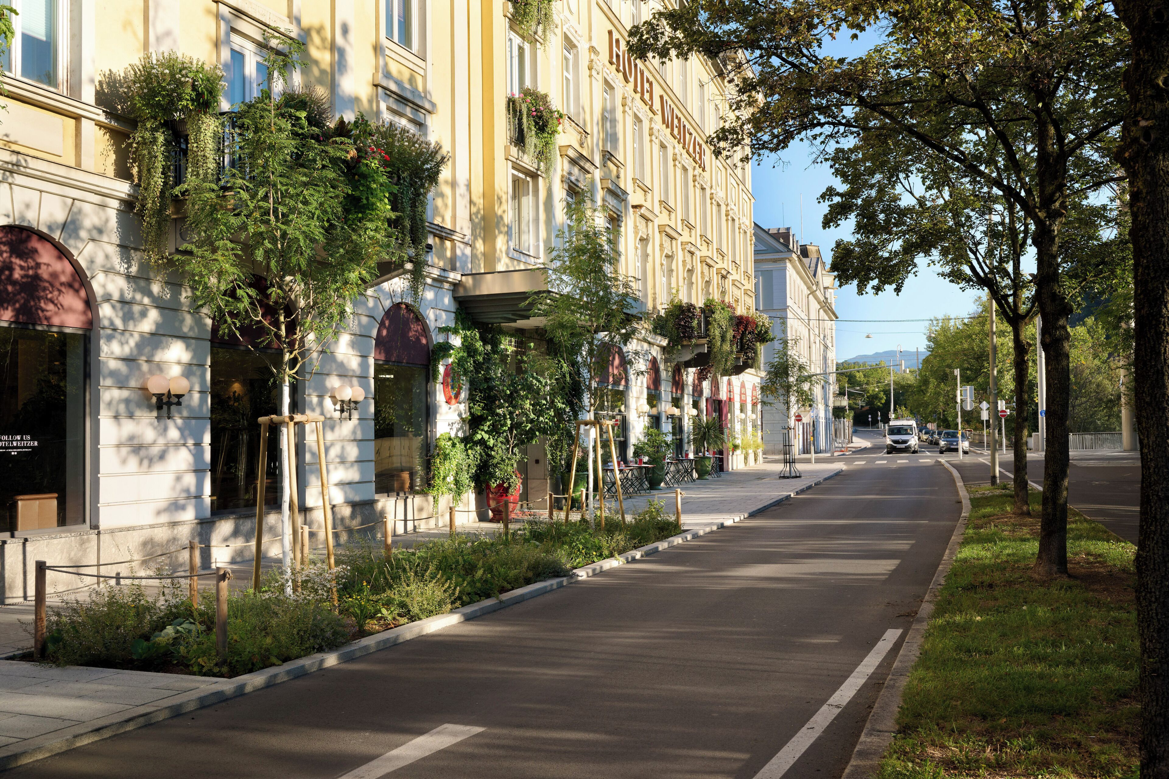 A street with a hotel named 'HOTEL WIELTER' on the left, featuring a row of windows with plants and a clear road.