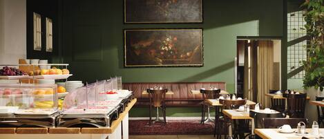 Un restaurant doté d’un mur végétal, de deux tableaux, d’un buffet proposant des fruits et des légumes, et d’un espace détente avec des tables et des chaises.