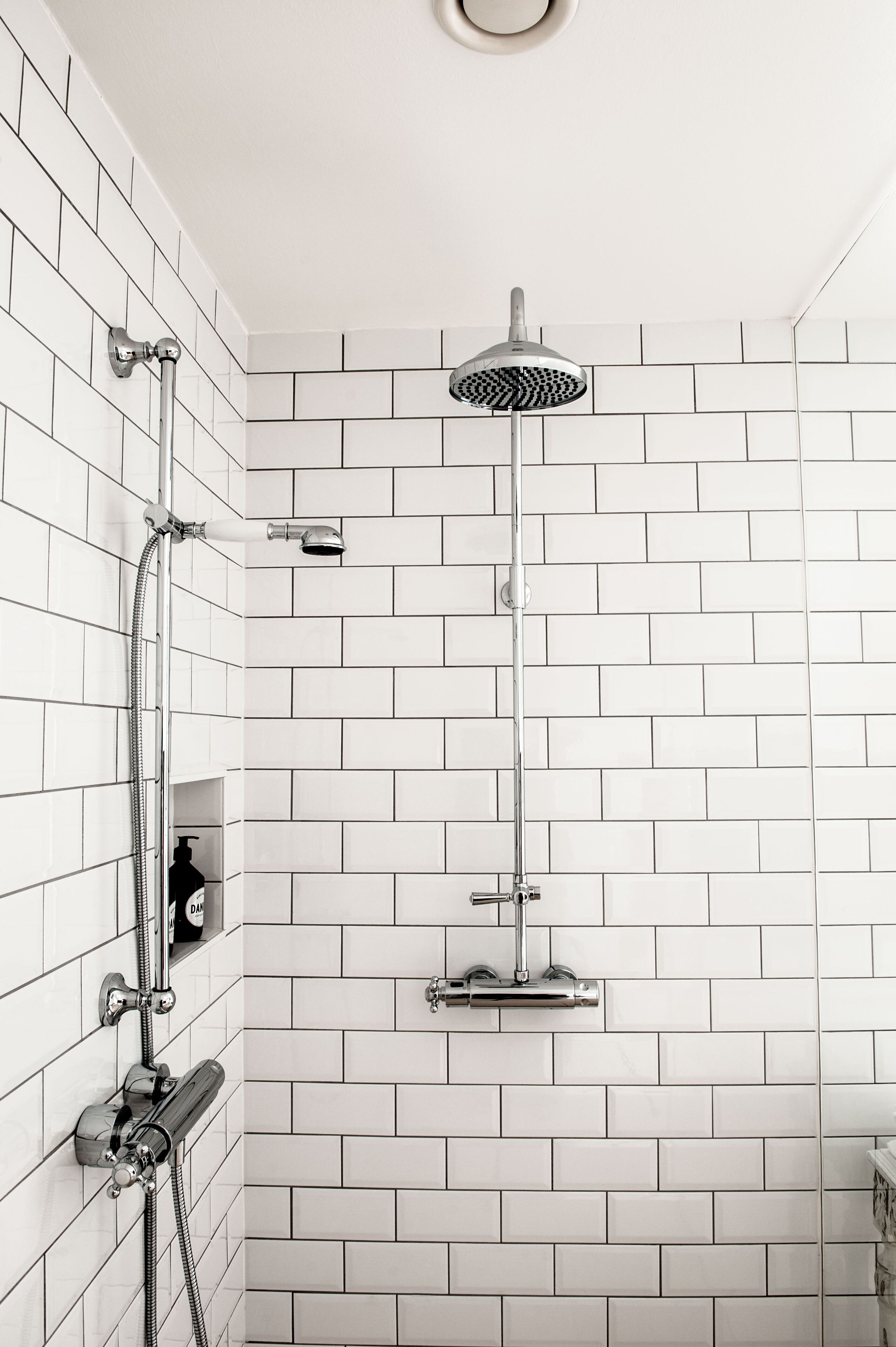 A modern bathroom with white subway tiles, a handheld showerhead, and a wall-mounted faucet.