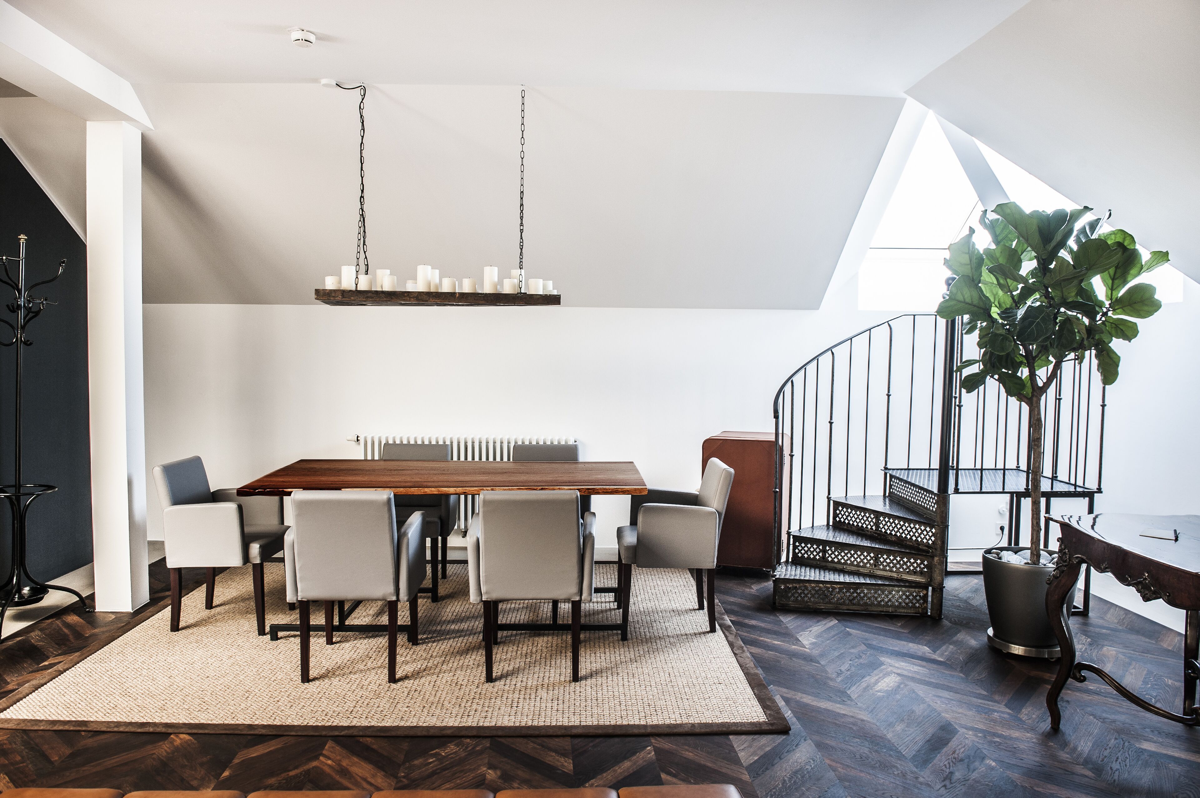 Un espace repas moderne avec une table en bois, six chaises, un luminaire suspendu et un escalier doté d’une rampe.