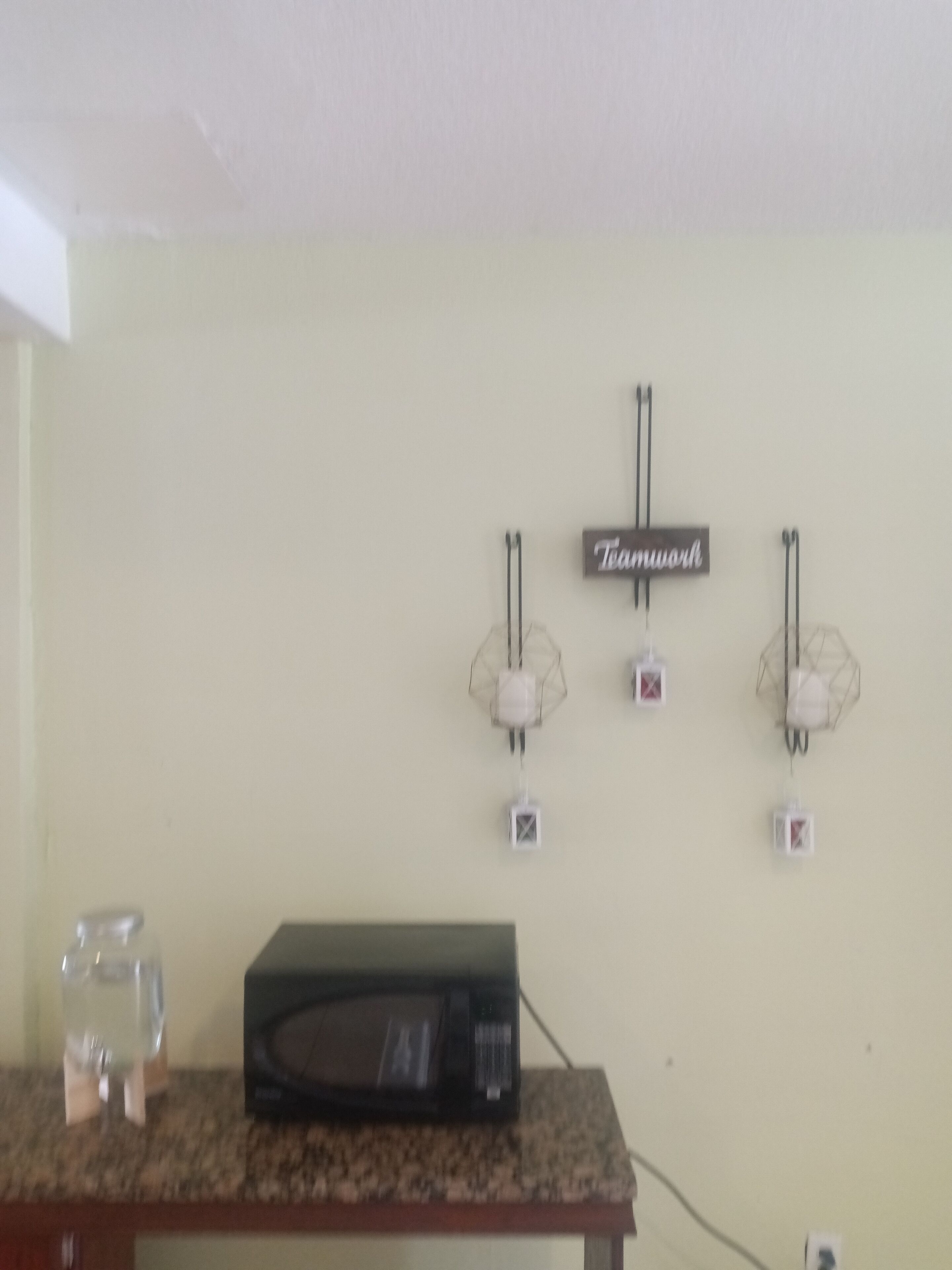 A kitchen with a microwave on a granite countertop, a glass of water, and wall-mounted light fixtures.