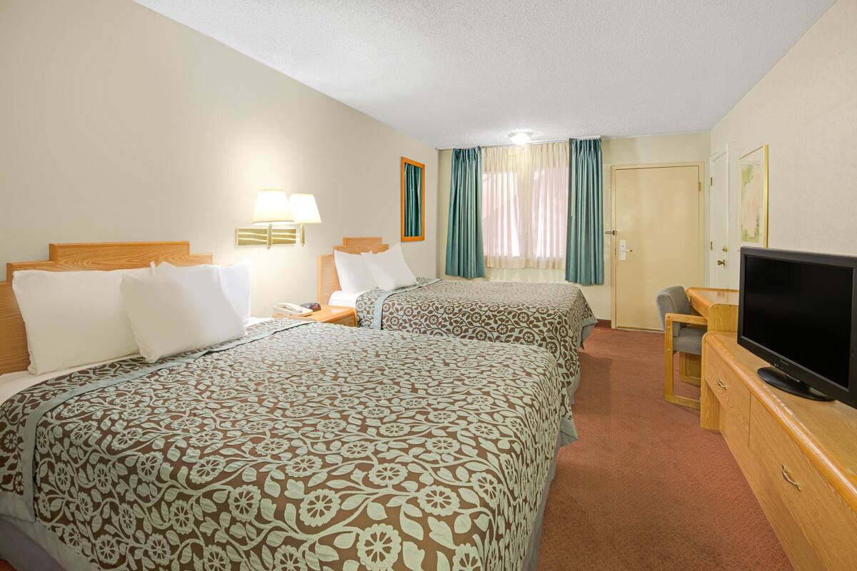 A hotel room with two beds, a TV, a desk, and a window with curtains.