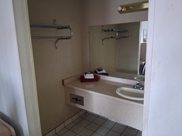 A bathroom with a sink, mirror, towel rack, and a towel dispenser.