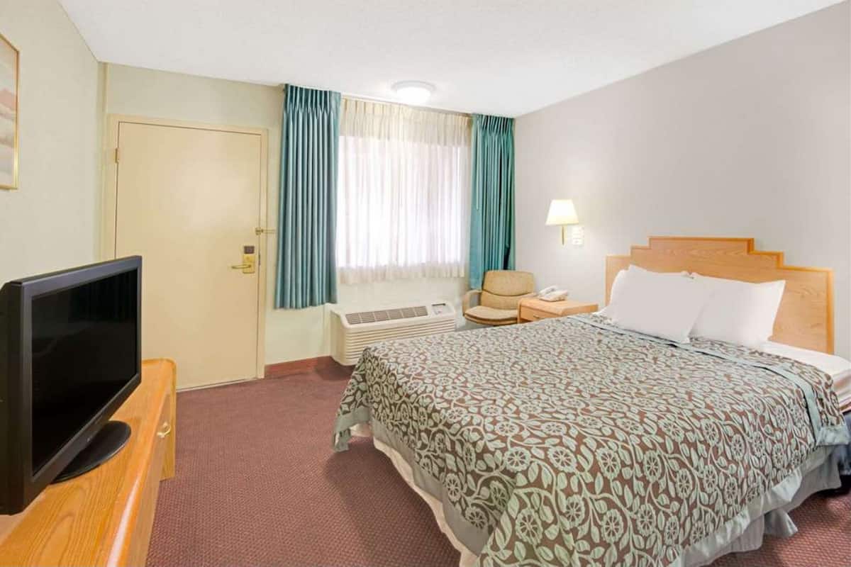 A hotel room with a bed, a television, a chair, a desk, and a window with curtains.