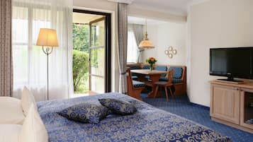 A hotel room with a large bed, a desk with a chair, a television, and a view of greenery outside.