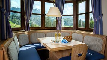 A cozy seating area with a table, benches, and a view of a mountainous landscape through large windows.