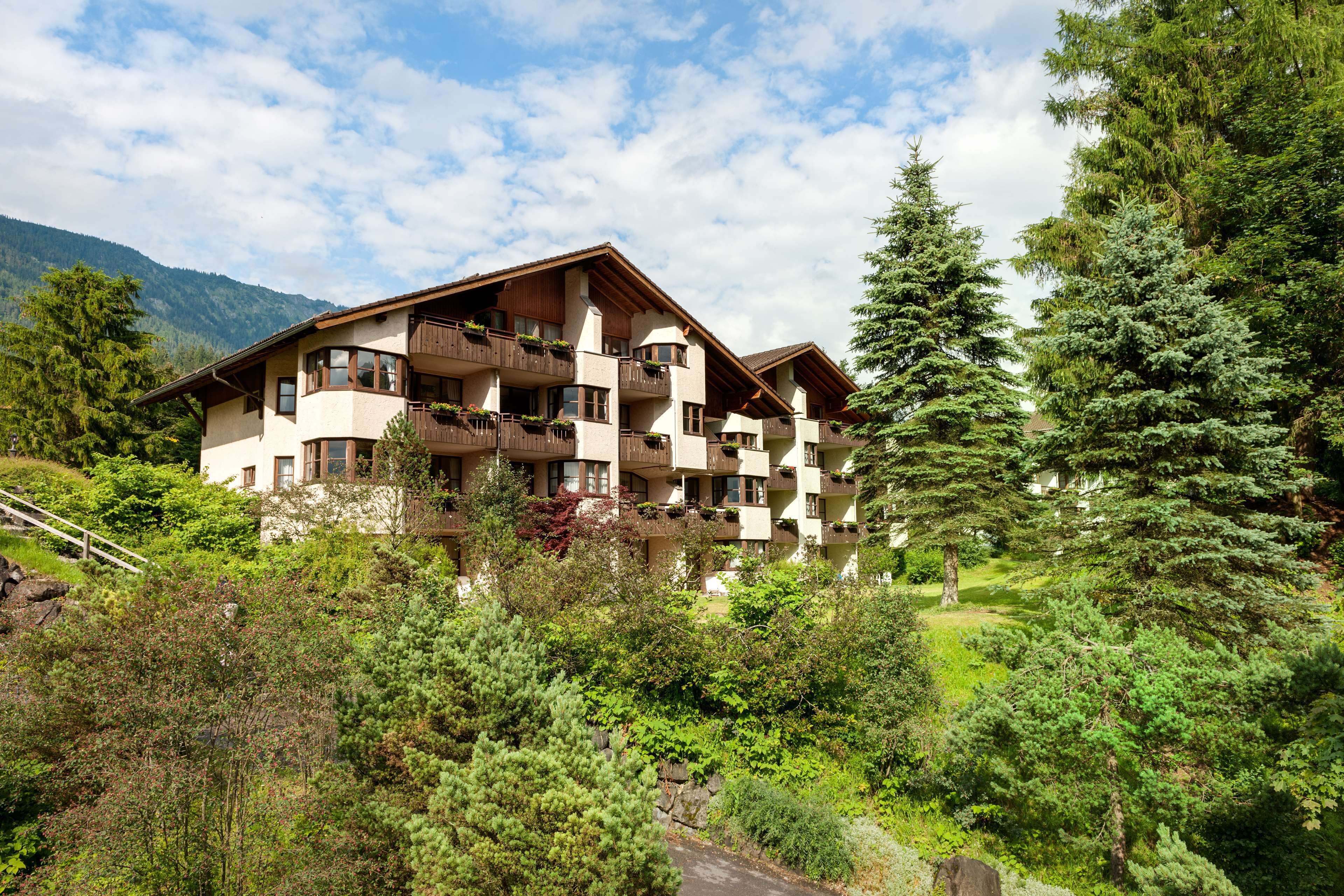 A multi-story hotel with balconies, surrounded by lush greenery and mountains.