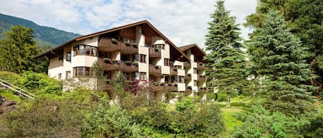 Un hôtel à plusieurs étages doté de balcons, entouré d’une végétation luxuriante et de montagnes.