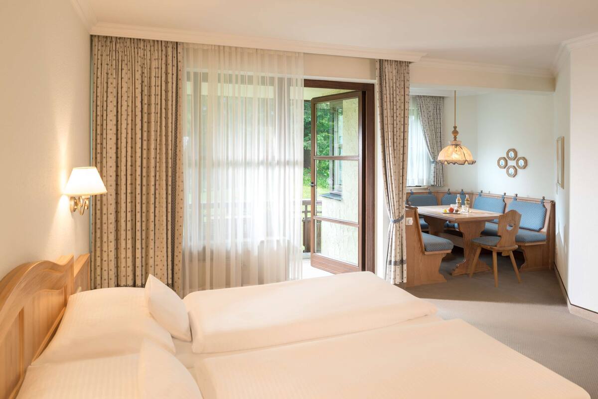 Une chambre d’hôtel avec un grand lit, un bureau avec des chaises, une fenêtre avec des rideaux et un luminaire suspendu.