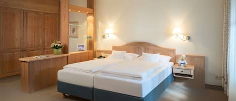 A hotel room with a double bed, wooden headboard, bedside tables, a mirror, and a small bedside lamp.