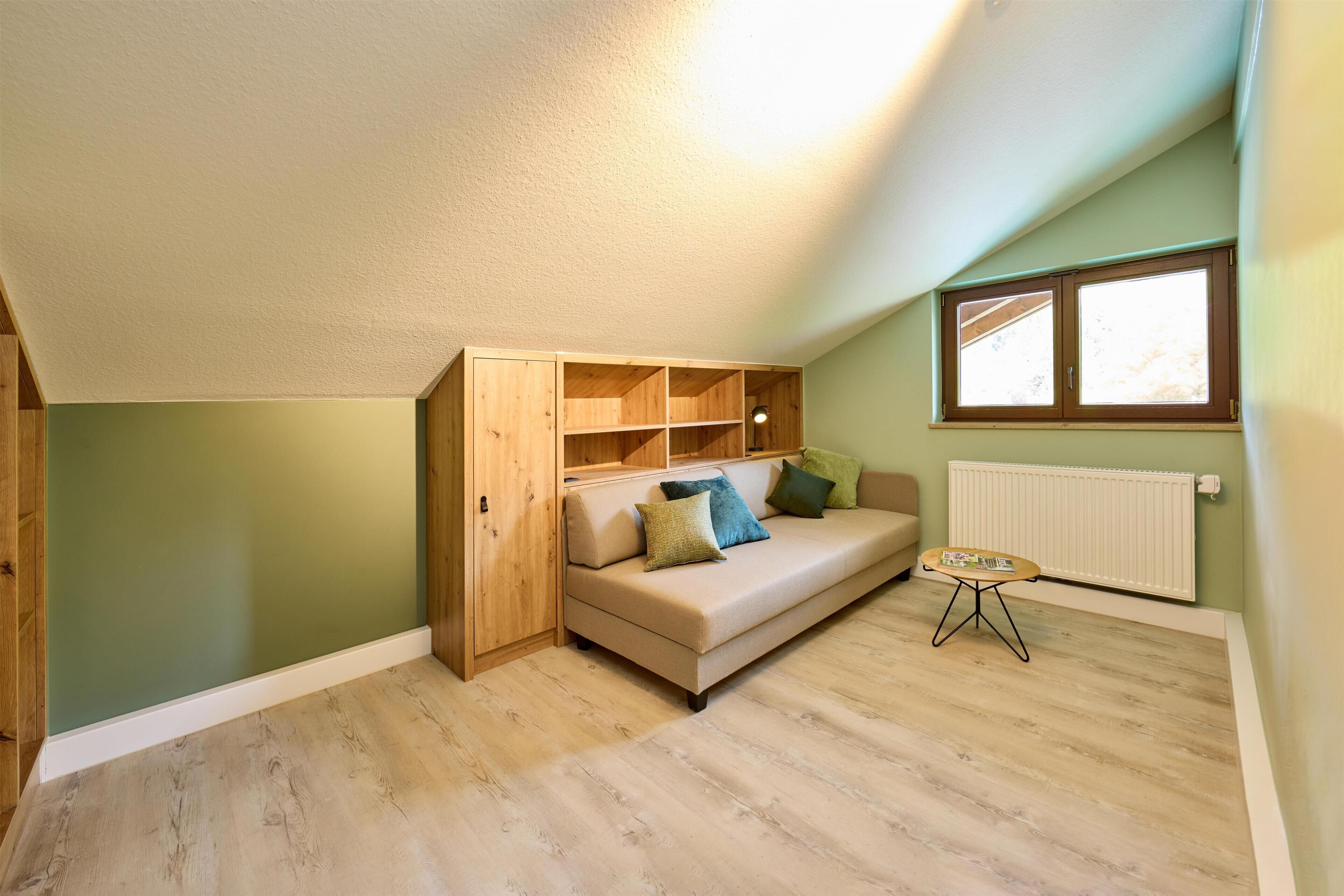 Ein Zimmer mit Hochbett, einer Couch, einem kleinen Tisch und einem Fenster.