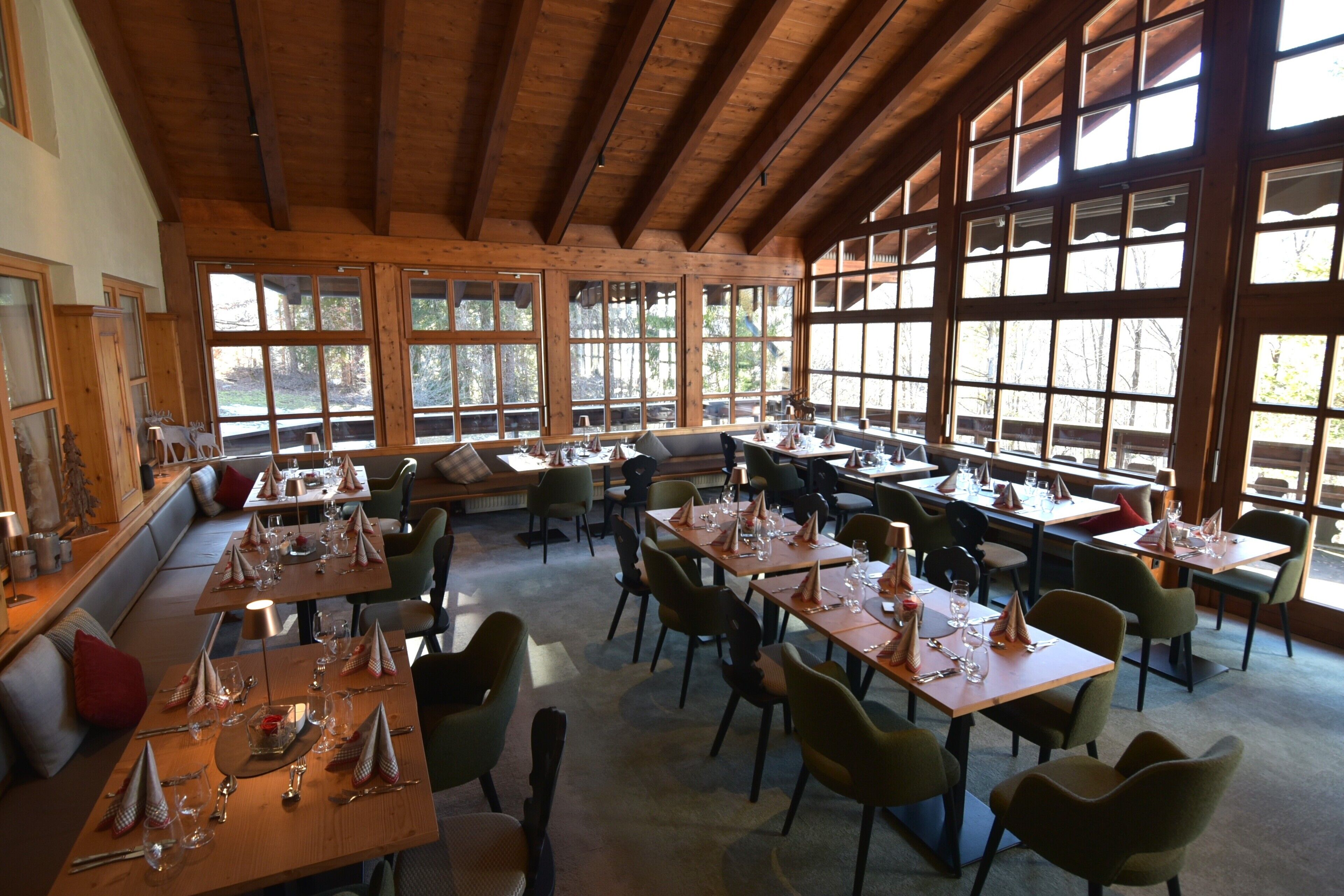 Uma sala de jantar ampla, com várias mesas e cadeiras, grandes janelas e vigas de madeira no teto.