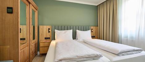 Habitación de hotel con dos camas, un armario de madera, una mesita de noche y una ventana con cortinas.