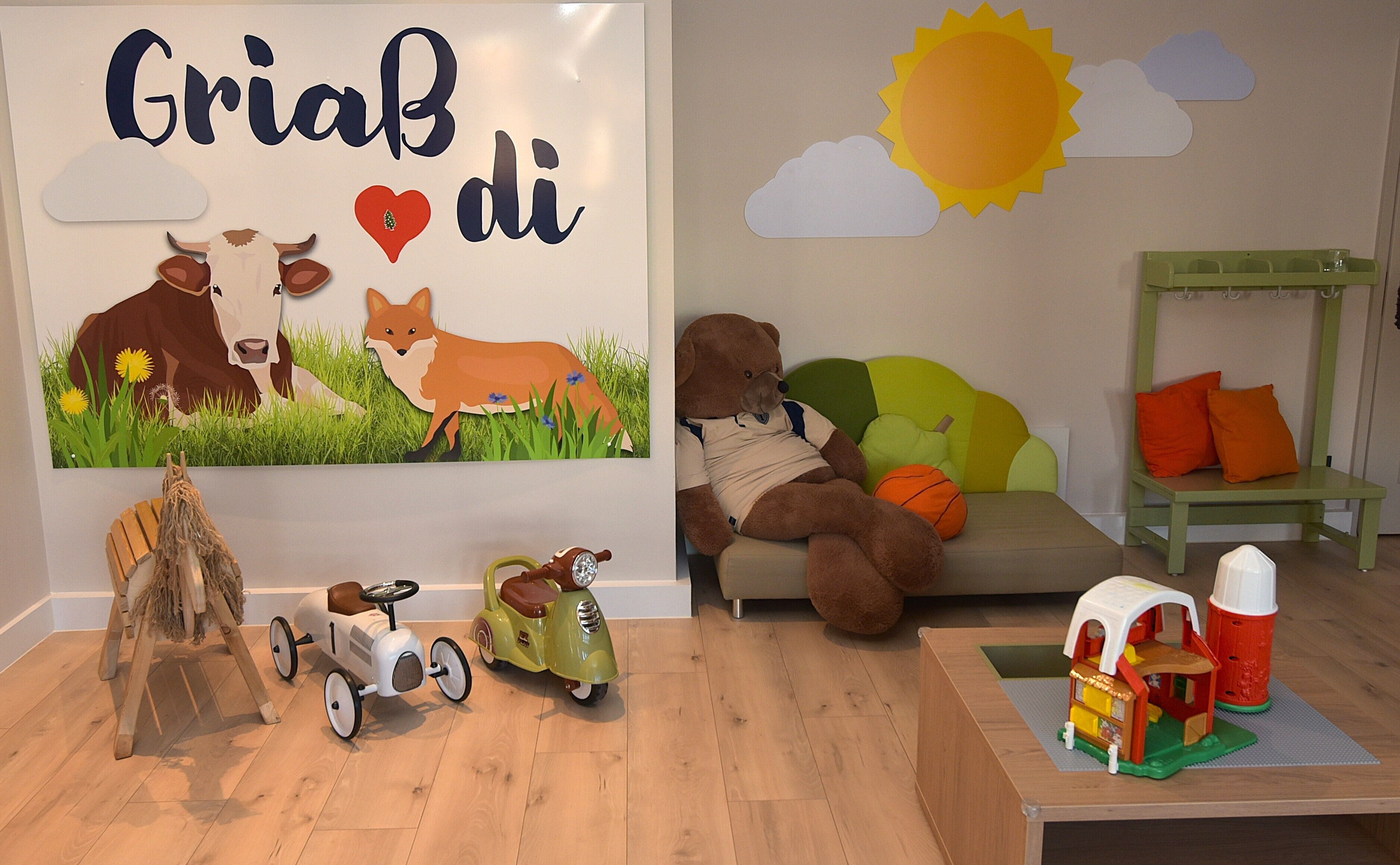 A children's playroom with a mural, a teddy bear, a scooter, and a toy house.