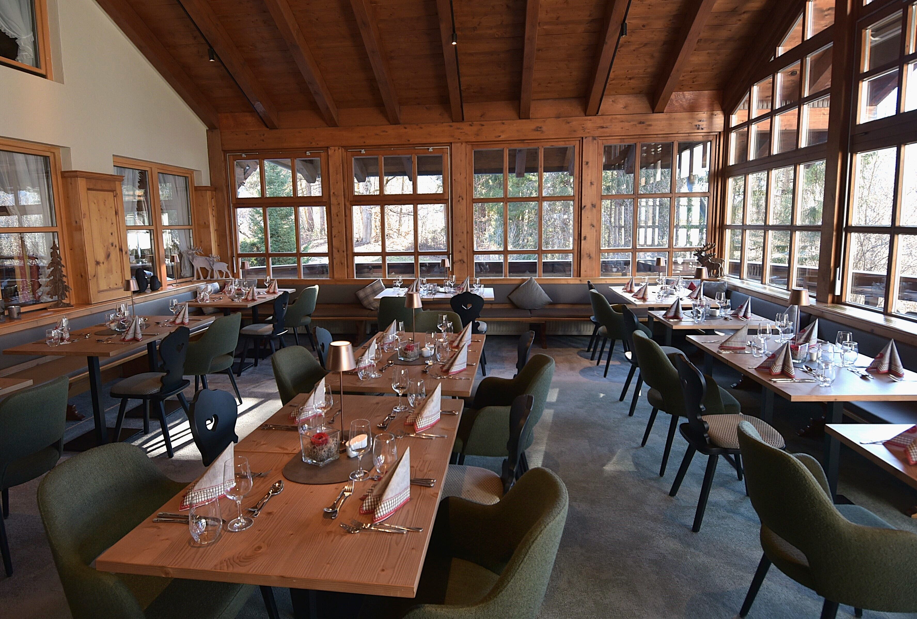 A dining area with wooden tables and chairs, large windows, and a high ceiling.