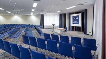 A conference room with rows of blue chairs, a projector screen, and a presentation area.