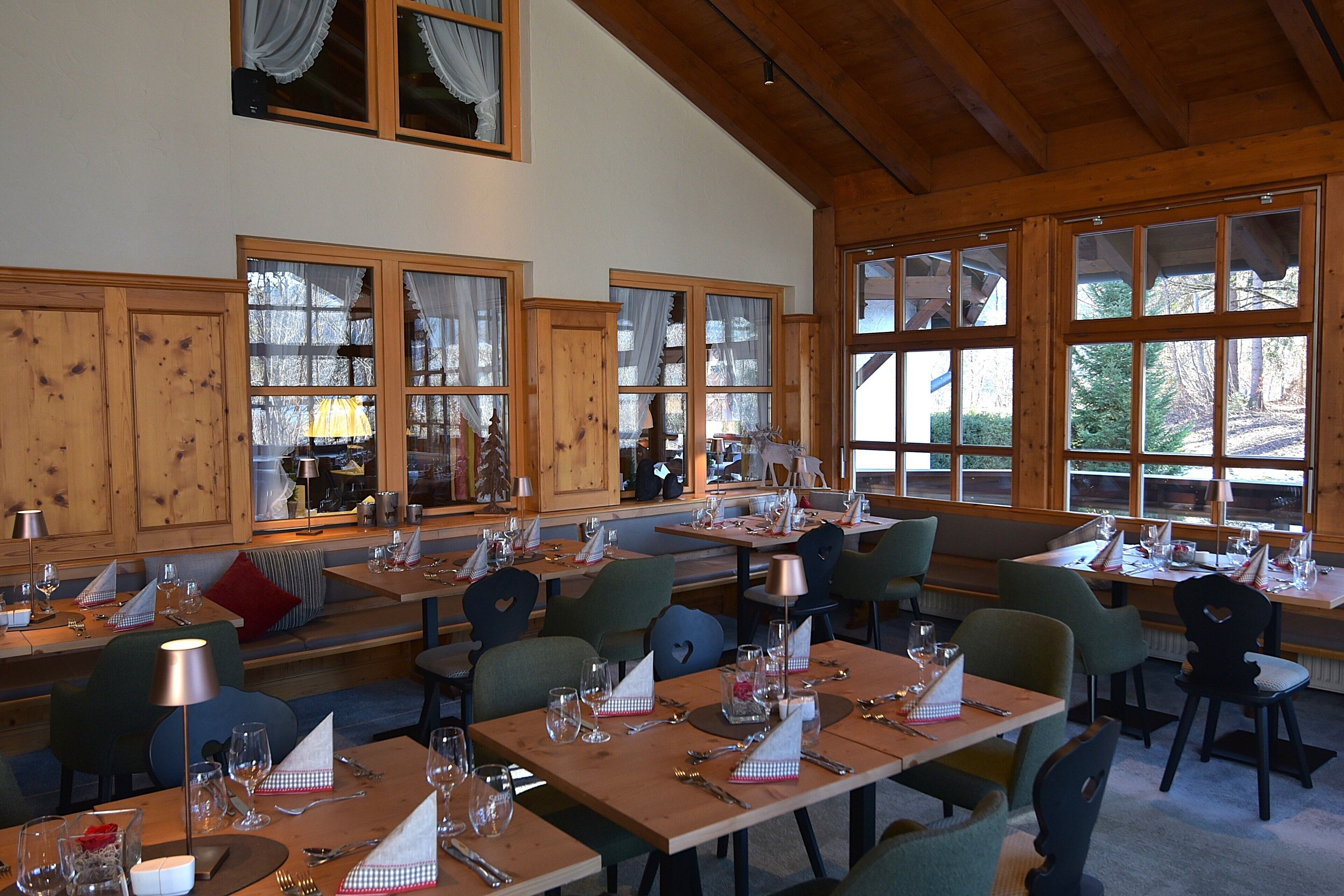 A restaurant with wooden interiors, large windows, and multiple dining tables set with tableware.