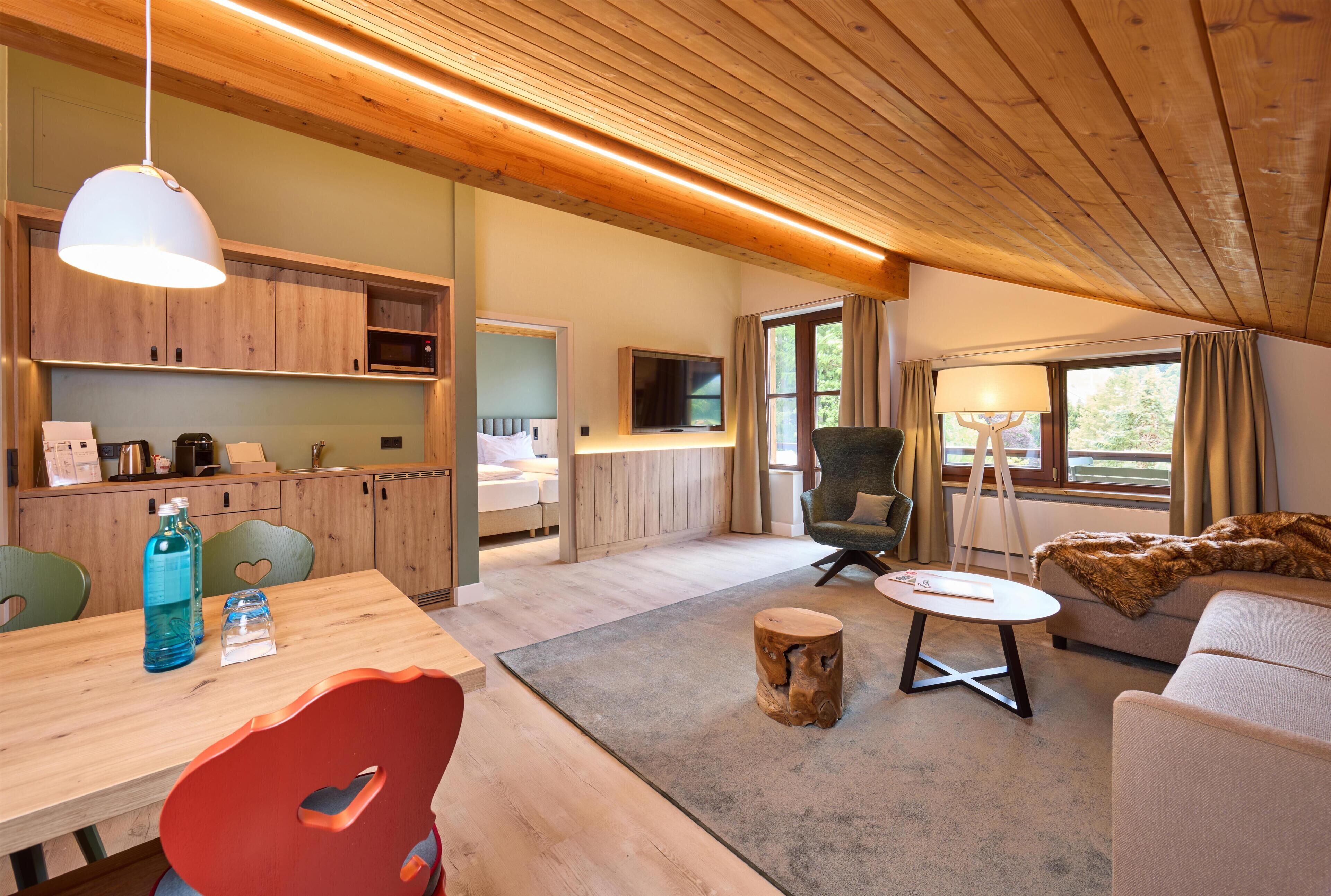 Un interior moderno con techo de madera, una zona de comedor con mesa y sillas, un sofá, un televisor y una ventana con cortinas.