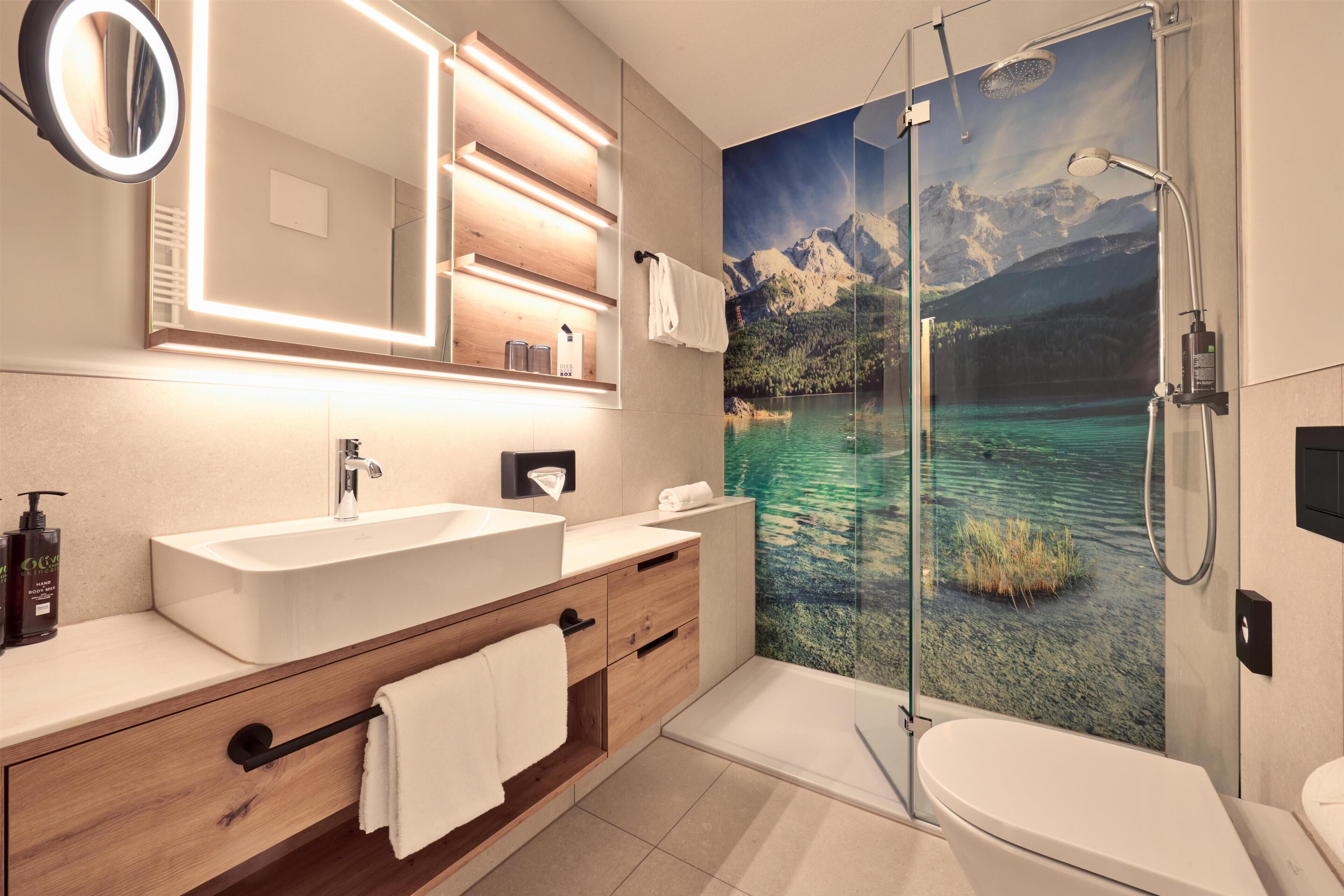 A modern bathroom with a large mirror, two sinks, a shower, and a toilet.
