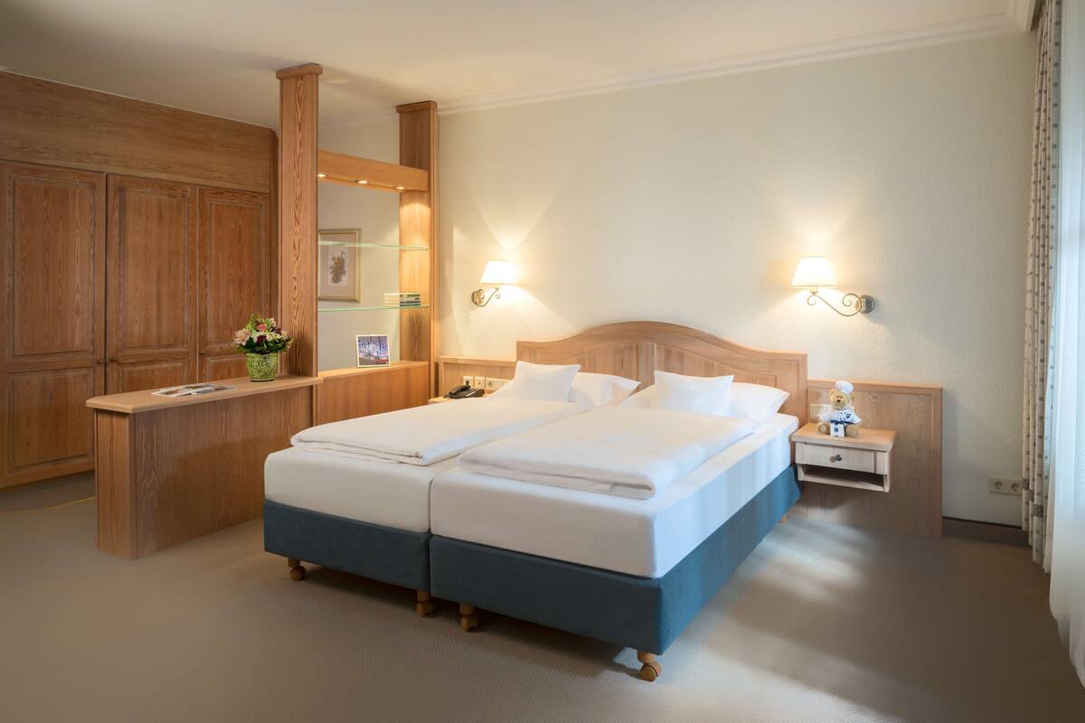 Un lit double avec une tête de lit en bois, deux tables de chevet avec des lampes, une armoire en bois et un miroir.
