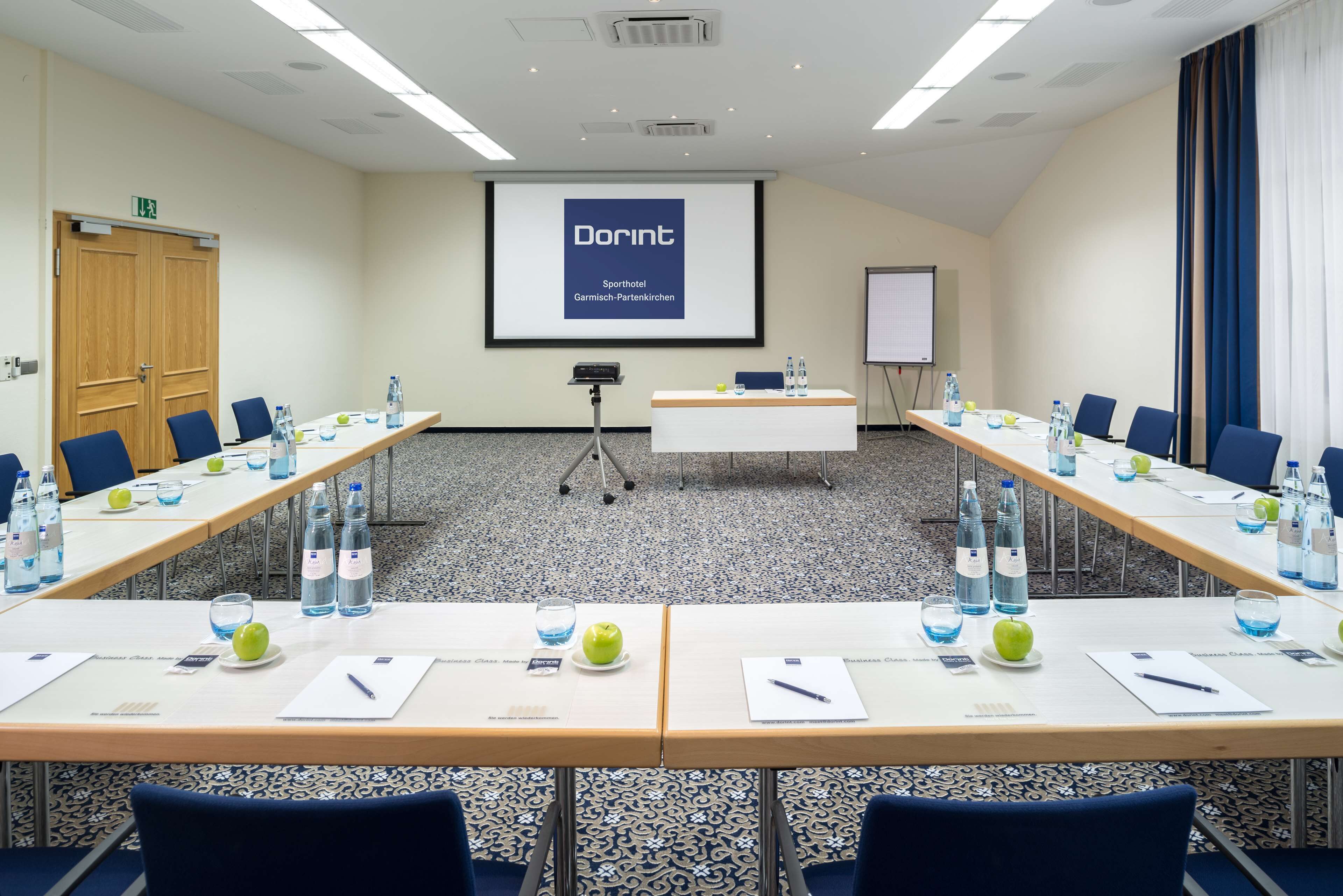 Un salón de conferencias con una pantalla grande mostrando 'Dorint' y 'Sporthotel Garmisch-Partenkirchen'.