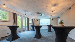 Un salón de conferencias con tres mesas negras, ventanas amplias y una pantalla de proyector mostrando 