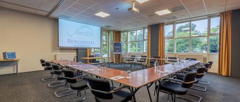 A conference room with a long table, chairs, a projector screen, and large windows with curtains.