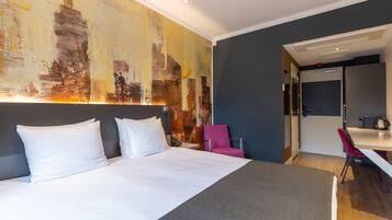 A hotel room with a large bed, a desk, a chair, and a painting on the wall.