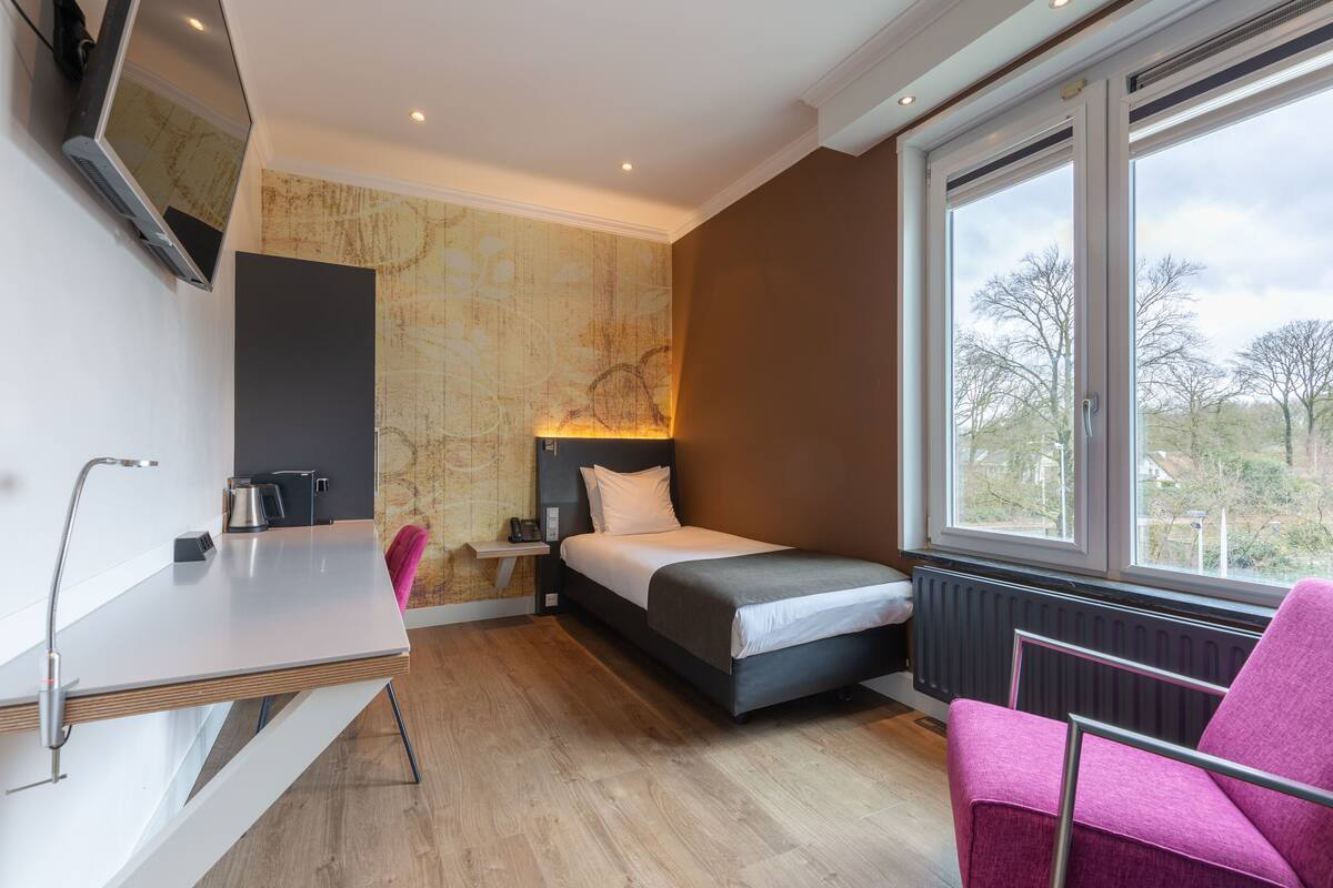 Una habitación de hotel moderna con cama, escritorio, silla y un ventanal grande.