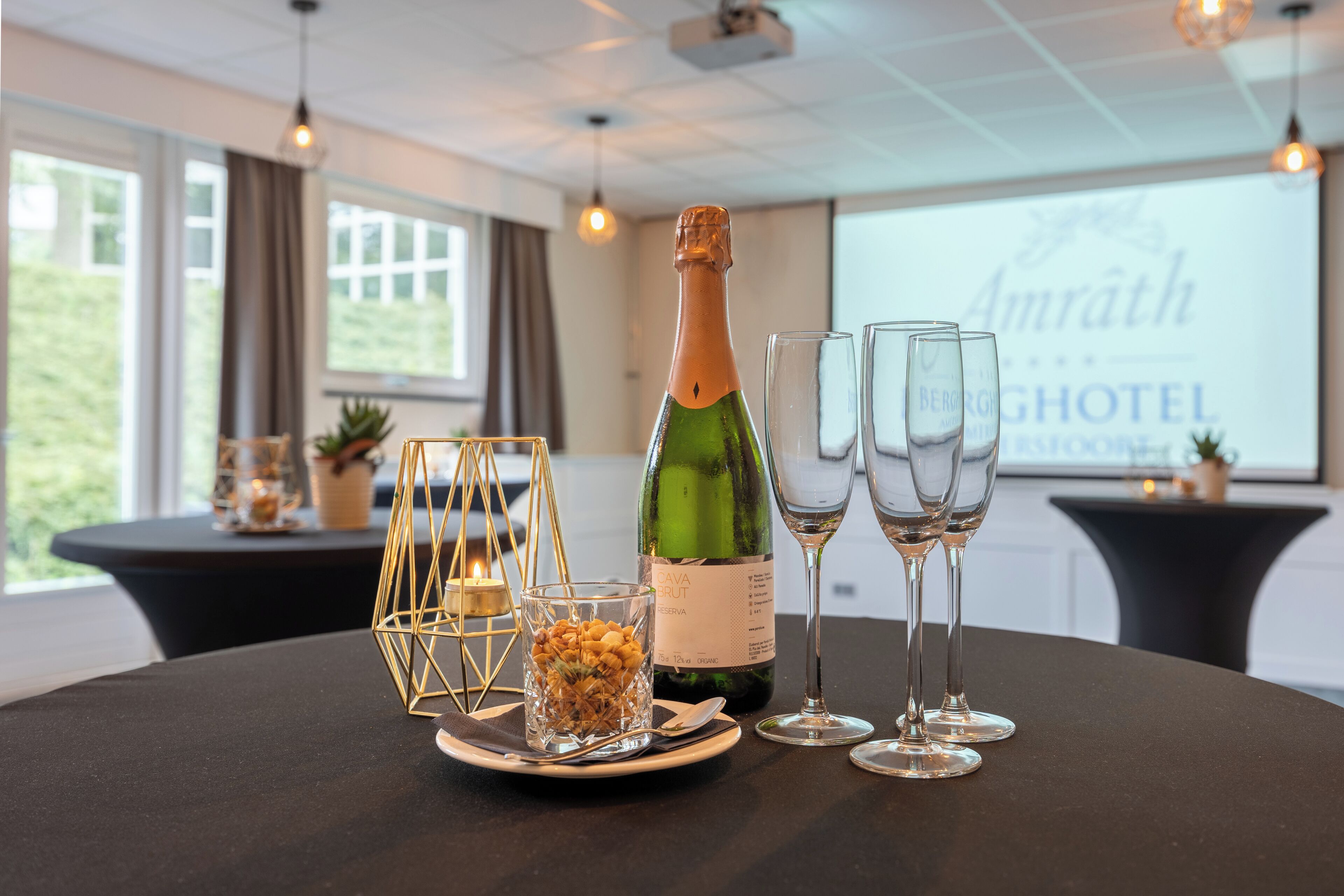 Una mesa con una botella de champán, dos copas, una copa con nueces y un candelabro geométrico dorado.