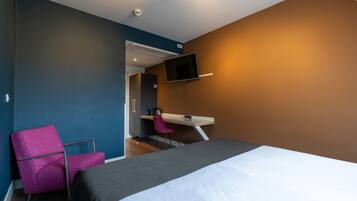 A modern hotel room with a bed, a desk, a chair, and a TV mounted on the wall.