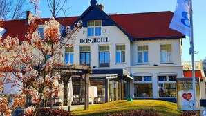Un hotel llamado "BERGHOTEL" con techo rojo, múltiples ventanas y un cartel en la fachada.