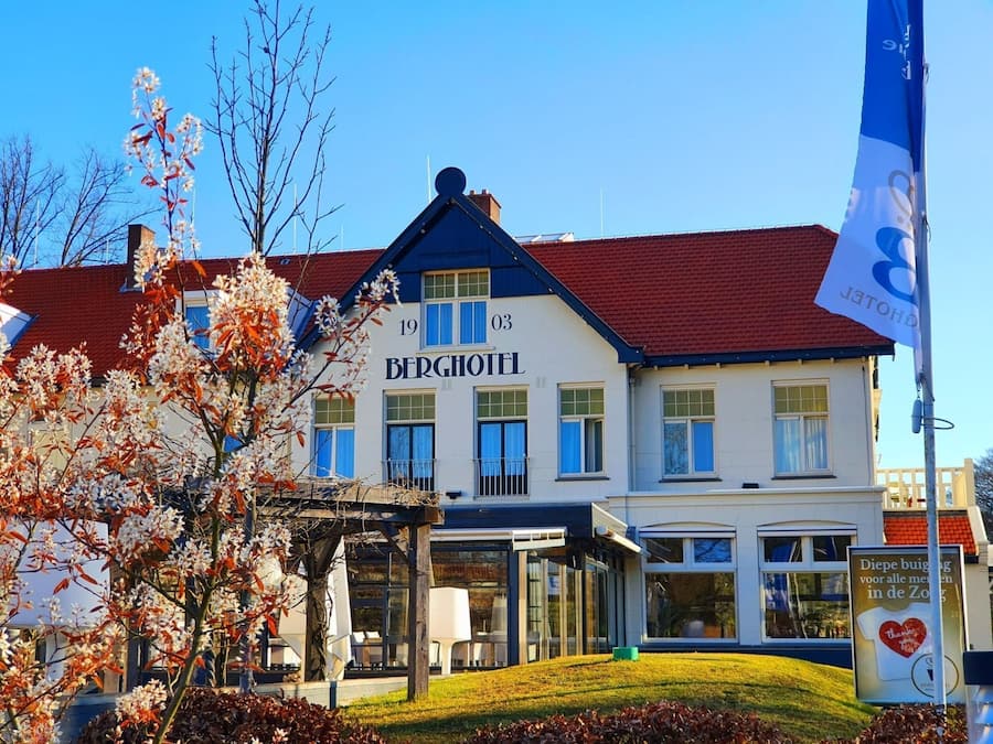 A hotel named "BERGHOTEL" with a red roof, multiple windows, and a signboard in front.