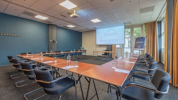 Un salón de conferencias con una larga mesa, sillas, una pantalla de proyector y una presentación sobre Amrath Berghotel Amersfoort.