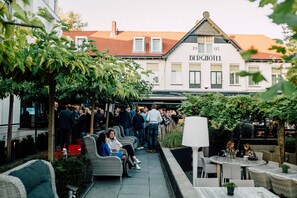 Relax in the charming outdoor seating area, surrounded by lush greenery and potted plants, near the entrance of the Berg Hotel.