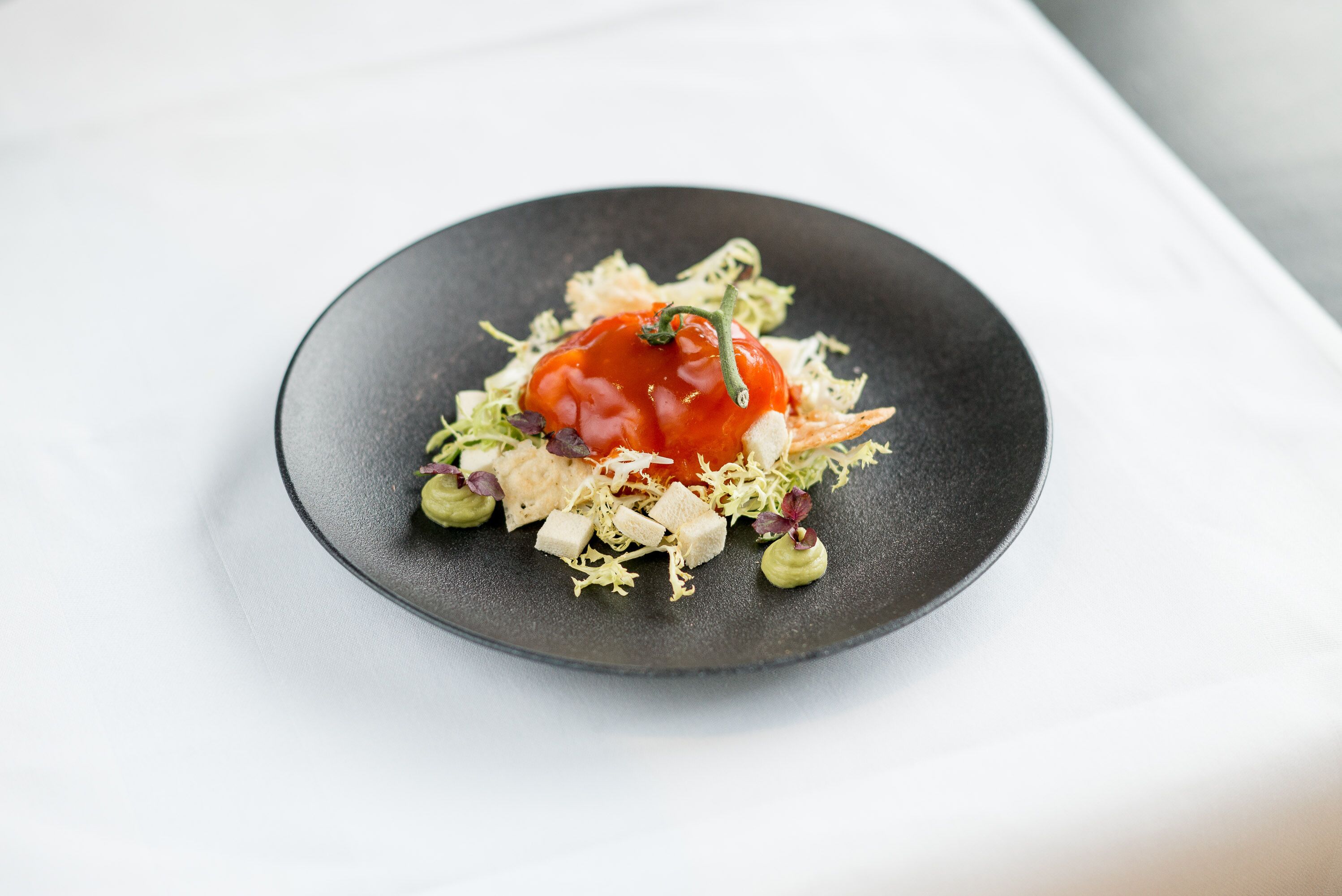 Un plato negro con ensalada sobre una superficie blanca.