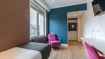 Een moderne hotelkamer met een bed, een roze stoel, een bureau en een aan de muur bevestigde televisie.