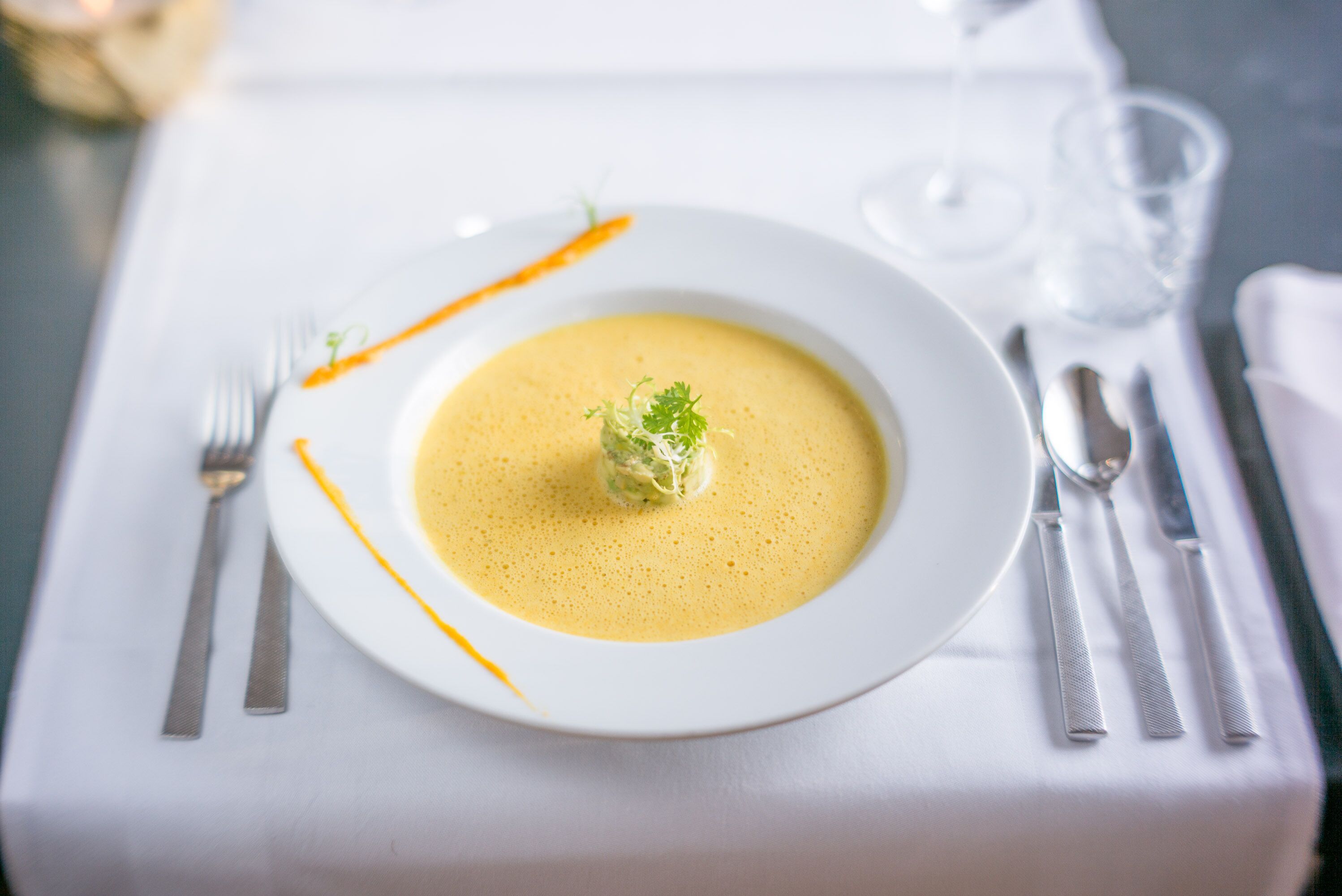 Un plato blanco con sopa y guarnición sobre una mesa con cubiertos.