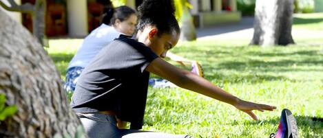 A person stretching outdoors on grass with trees and a building in the background.